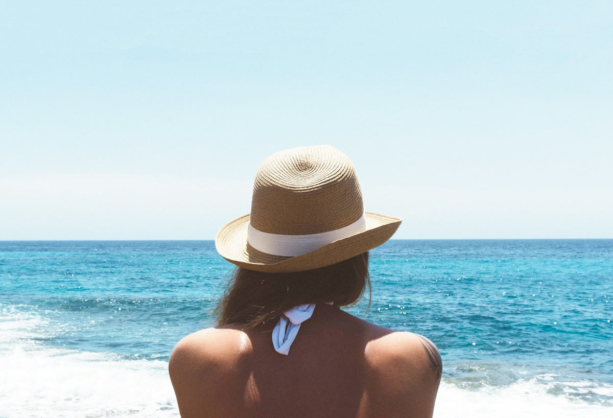 Woman in a sun hat looking out at the ocean, illustrating sun exposure and skin pigmentation in the melanotan 1 vs 2 comparison