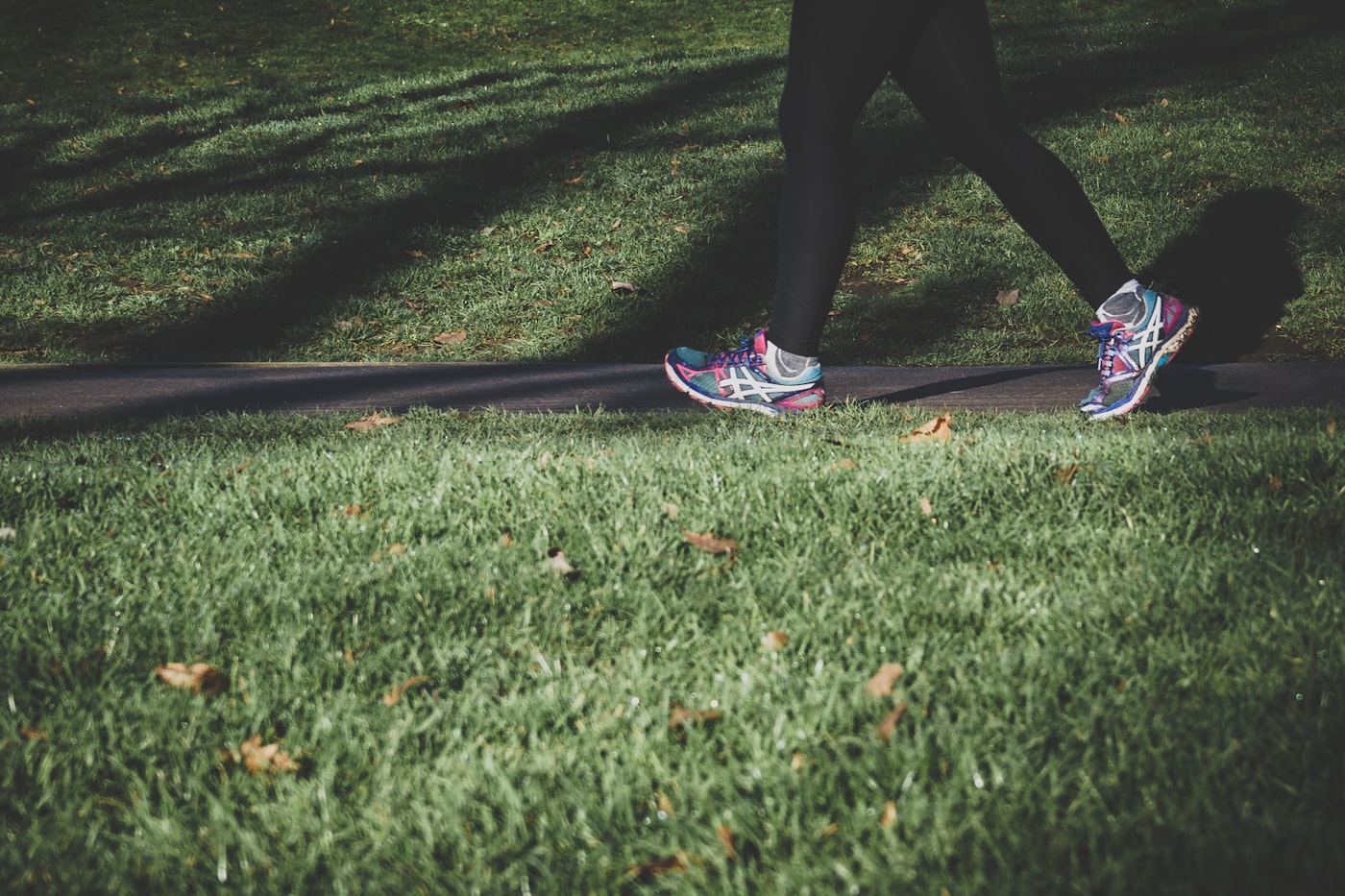 Person walking briskly on a sunlit park path in athletic shoes