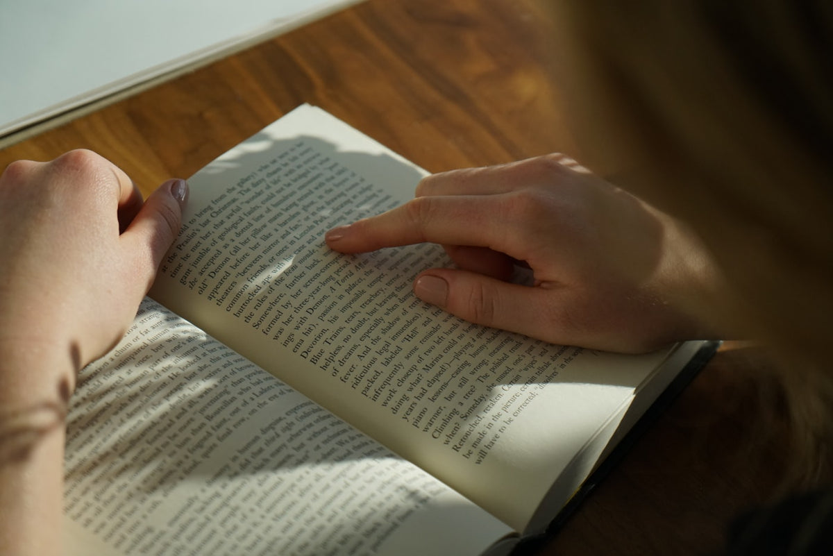 person reading book on brown wooden table taken at daytime