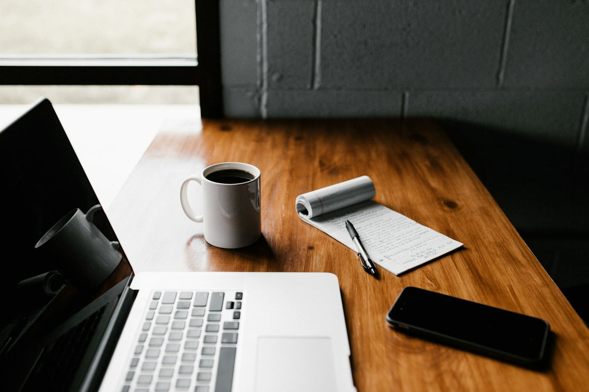Laptop, coffee mug and notepad on a wooden desk, set up for reviewing a peptide certificate of analysis