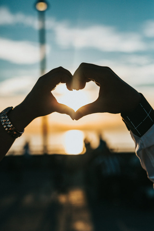 Two hands forming a heart shape against a sunset sky, illustrating PT-141 drug interactions and sexual wellness safety