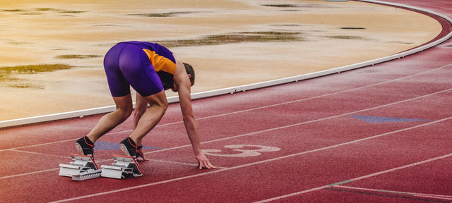 Sprinter crouched in the starting blocks on a red running track, illustrating athletic performance in context of ipamorelin cortisol research