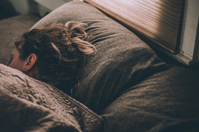 Person sleeping peacefully under a quilt in a dim bedroom, illustrating deep sleep vs REM sleep and hormone recovery