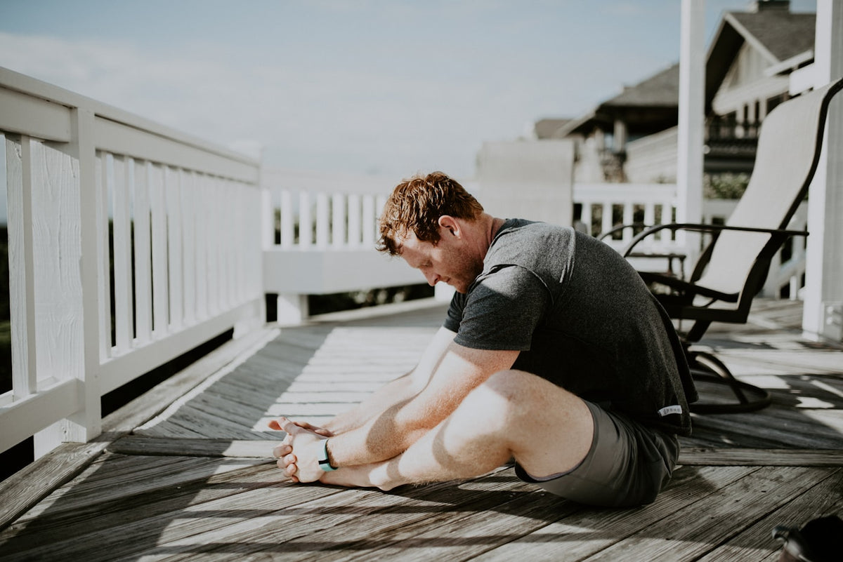 Man stretching and doing recovery mobility work outdoors on a home porch