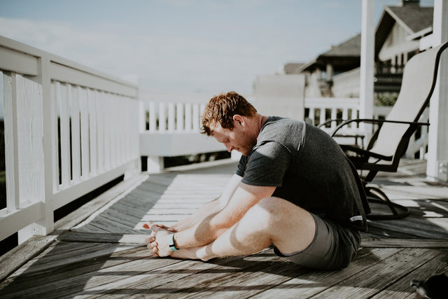 Man stretching and doing recovery mobility work outdoors on a home porch
