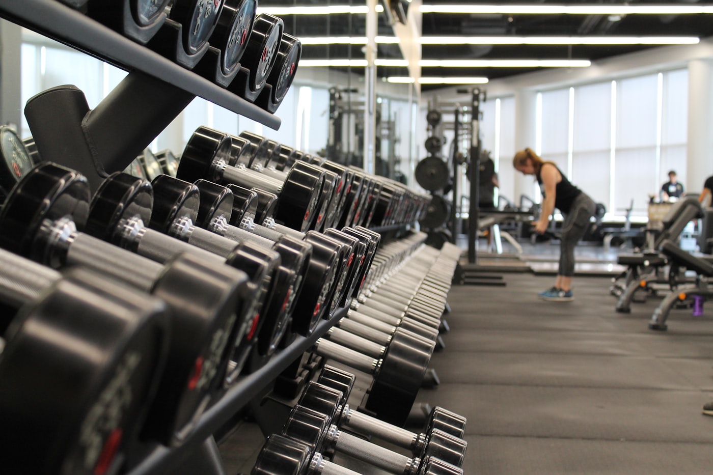 Row of dumbbells in a modern gym with a person training in the background — resistance training for muscle health and longevity