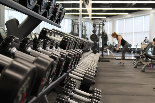 Row of dumbbells in a modern gym with a person training in the background — resistance training for muscle health and longevity
