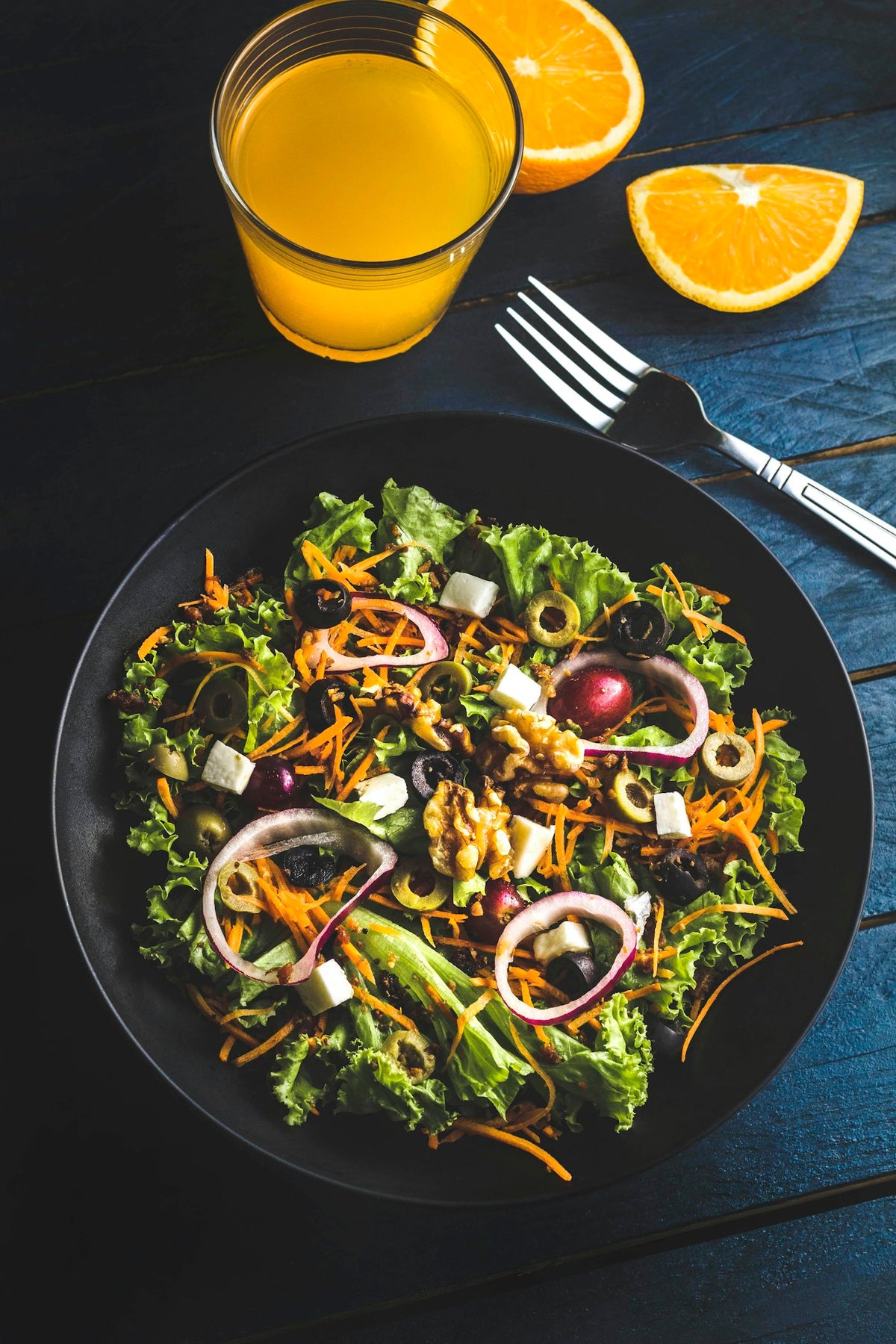 Fresh salad with walnuts and olives beside a glass of orange juice, illustrating mealtime fullness signals in amylin vs GLP-1