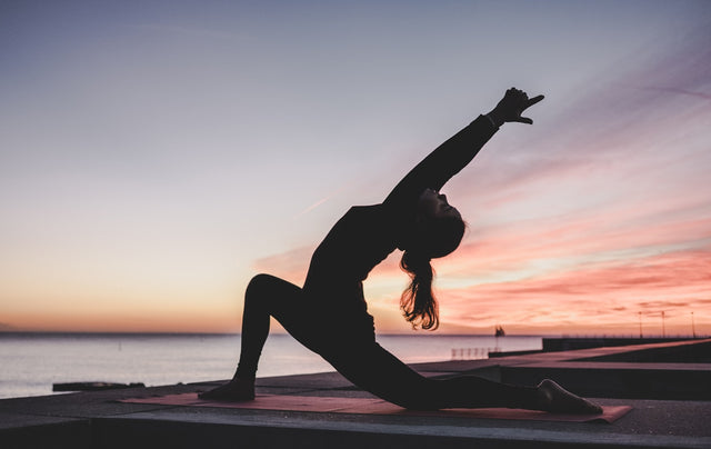 Silhouette of person doing yoga at sunset by the ocean, calm mindful wellness