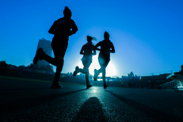 Three runners silhouetted against a bright blue sunrise sky on an outdoor track, representing steady progress through a tirzepatide plateau