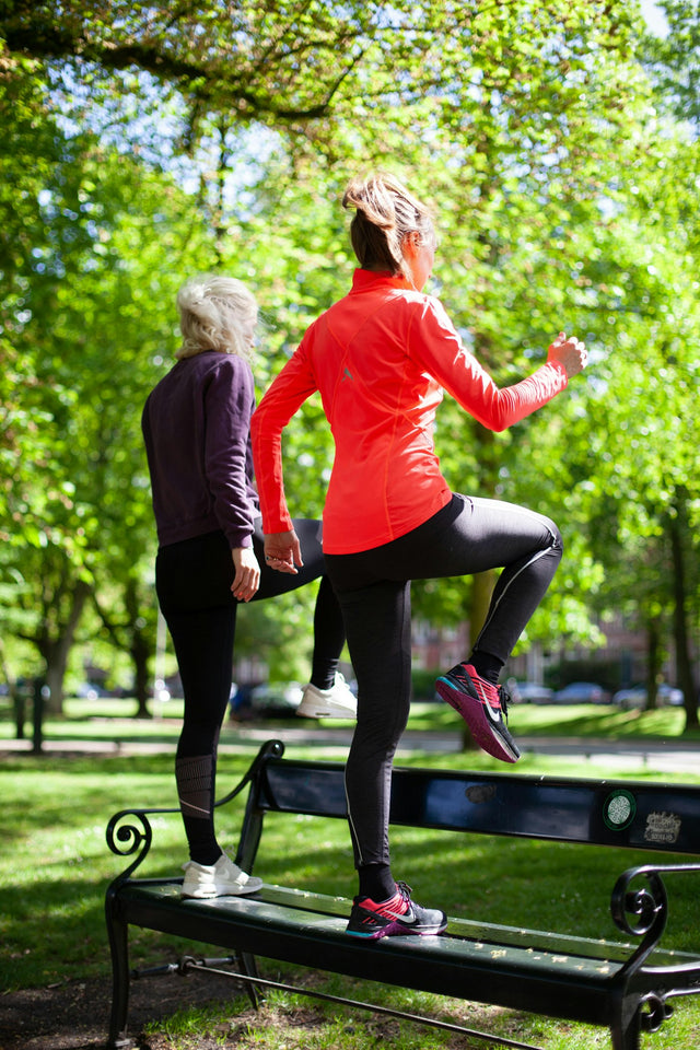 photography of women standing on black bench near outdoor during daytime