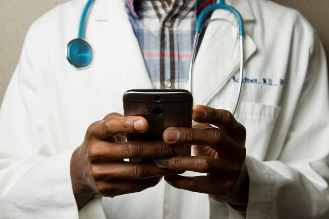 person wearing lab coat with green stethoscope on neck using phone while standing