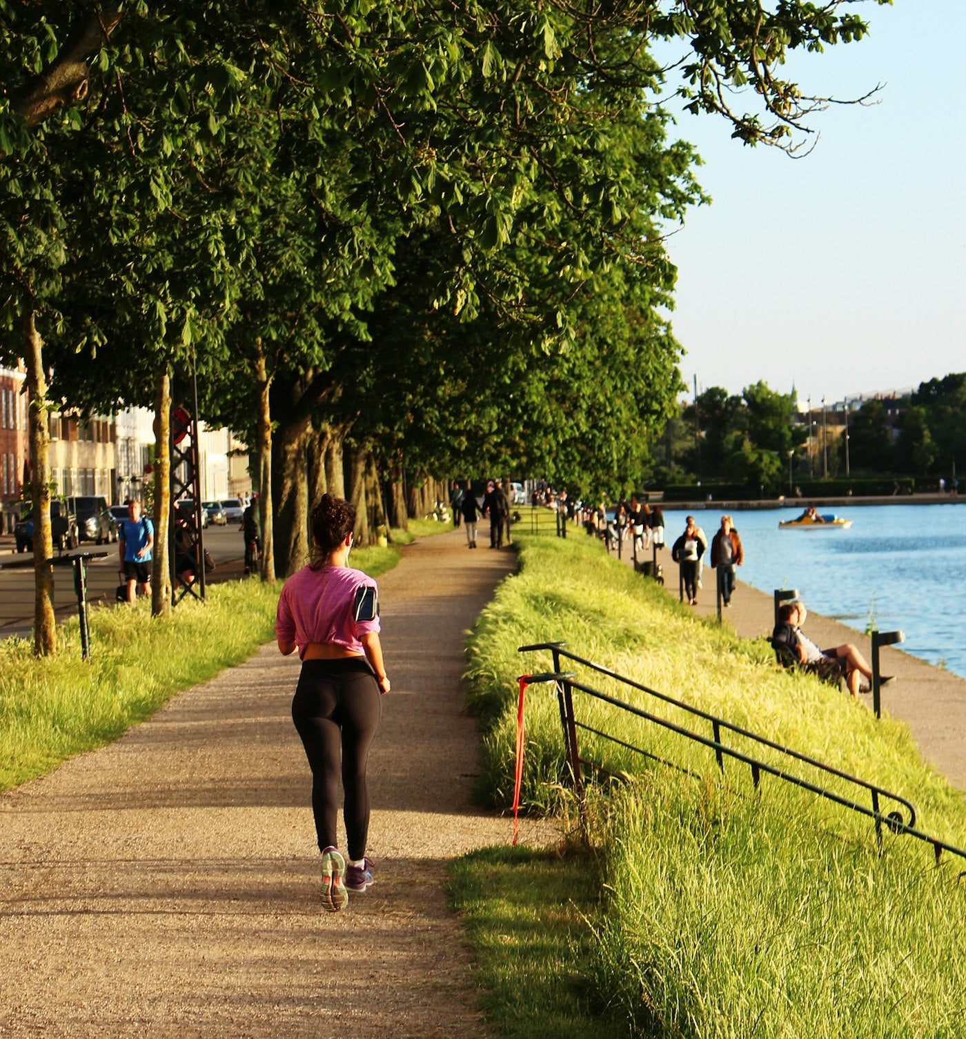 Woman jogging on a tree-lined waterfront path in natural light, healthy active lifestyle