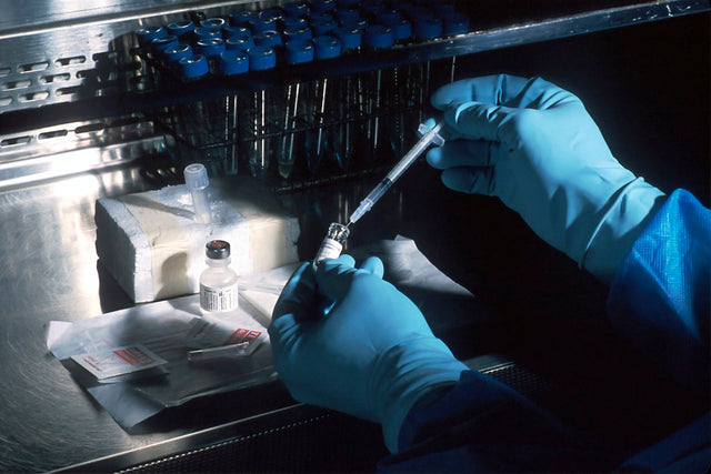 Gloved hands drawing medication from a vial with a syringe