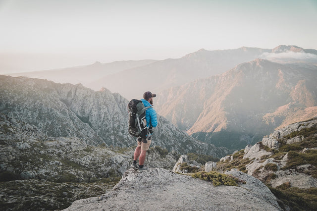 Man hiking with a backpack on a dramatic mountain summit, representing vitality and active health goals