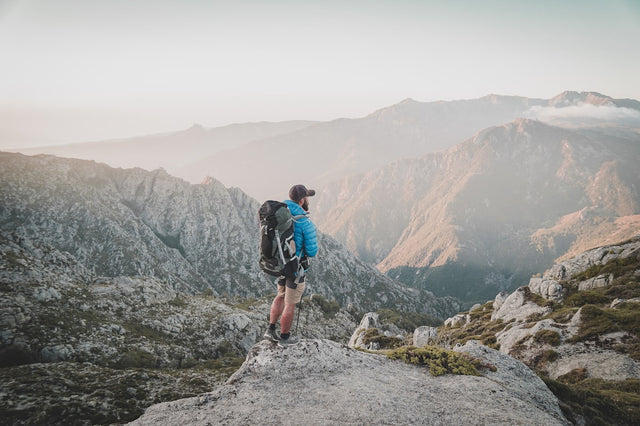 Hiker standing on a rocky mountain peak at sunset, representing active aging and longevity