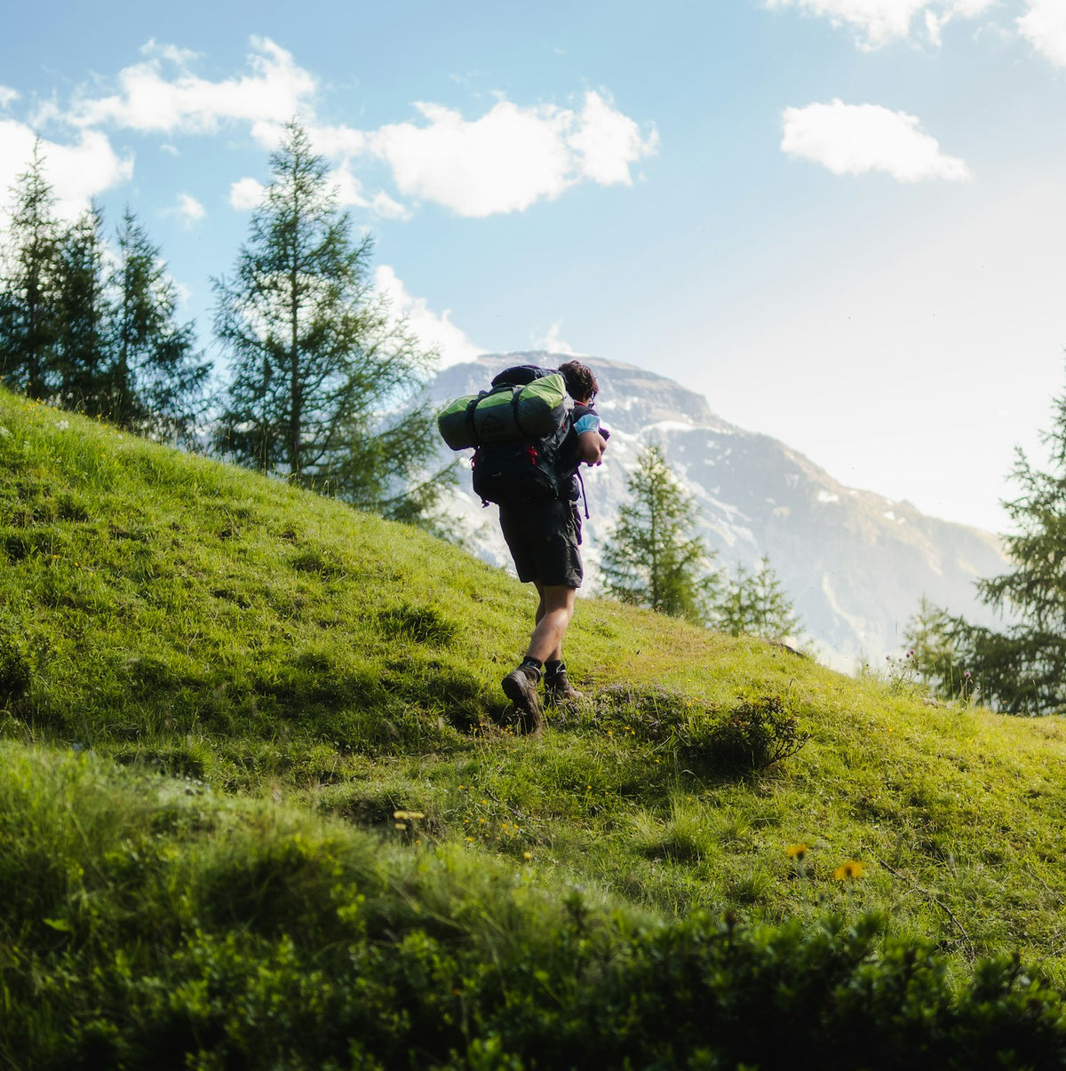 Man hiking up a green mountain slope with a backpack, representing active cardiovascular health on TRT