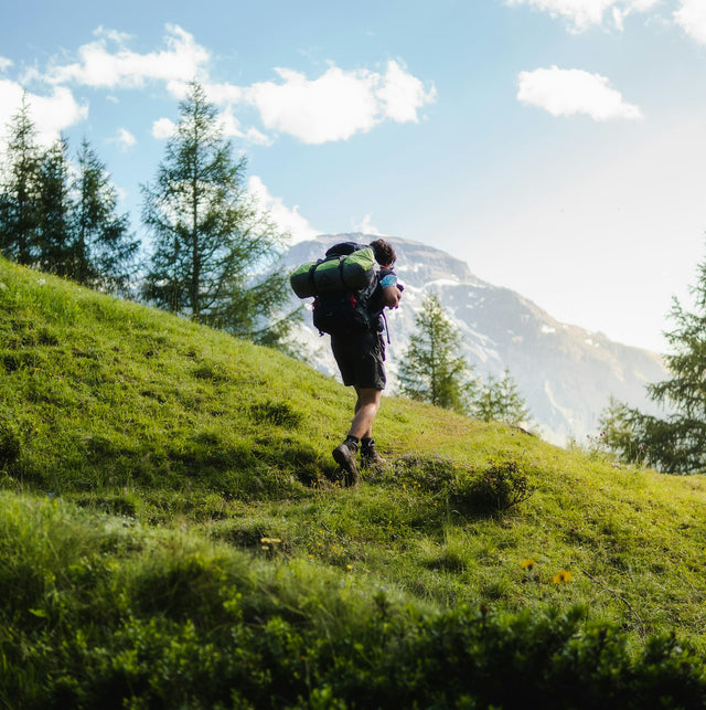 Man hiking up a green mountain slope with a backpack, representing active cardiovascular health on TRT