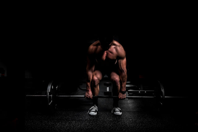 shirtless man lifting barbell in gym