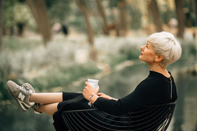 Mature woman relaxing outdoors with coffee, representing wellness and hormone optimization