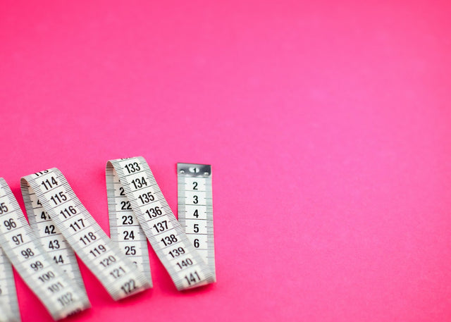 A group of measuring tape on a pink surface, representing weight-loss tracking