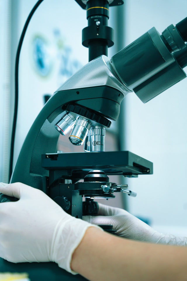 Gloved hand operating a microscope in a laboratory