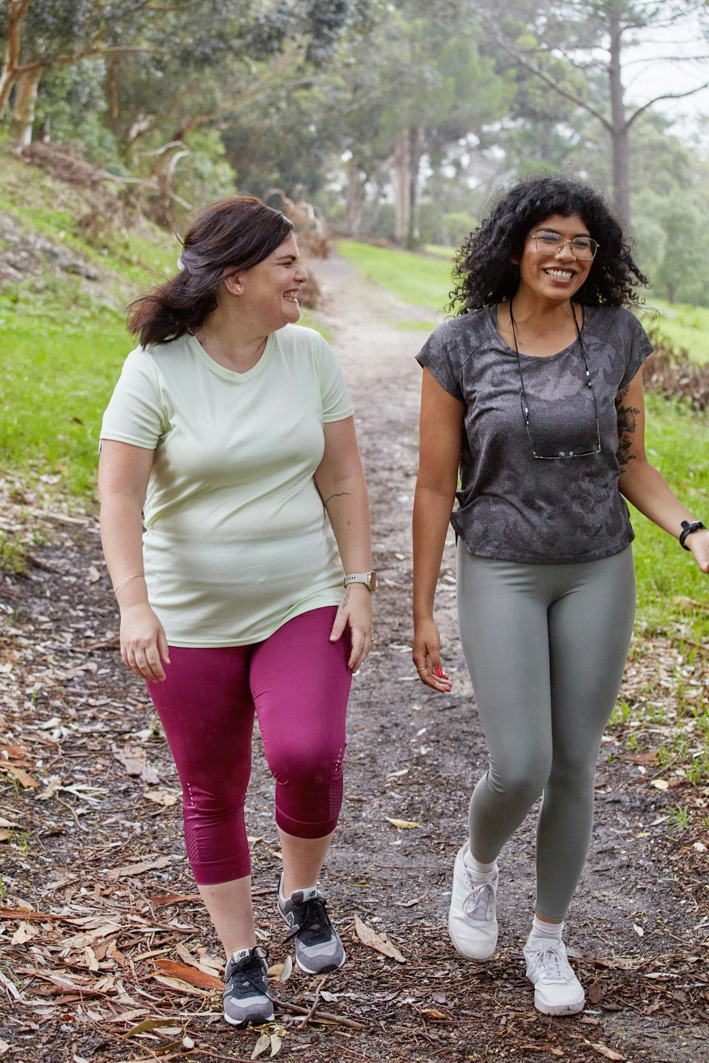 Two women walking together on a wooded path in active wear on a bright day