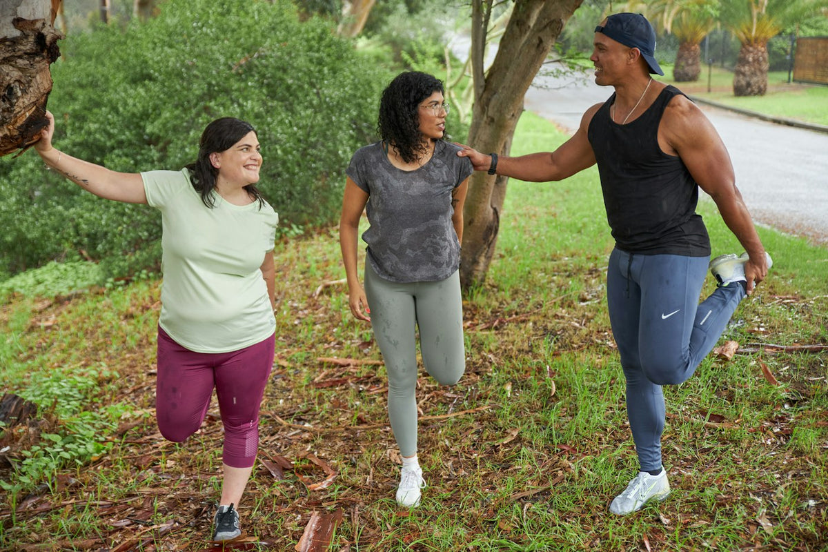 Three friends stretching their legs outdoors before a run, illustrating joint health and recovery
