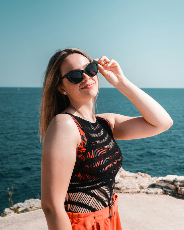 a woman wearing sunglasses standing on a beach next to the ocean