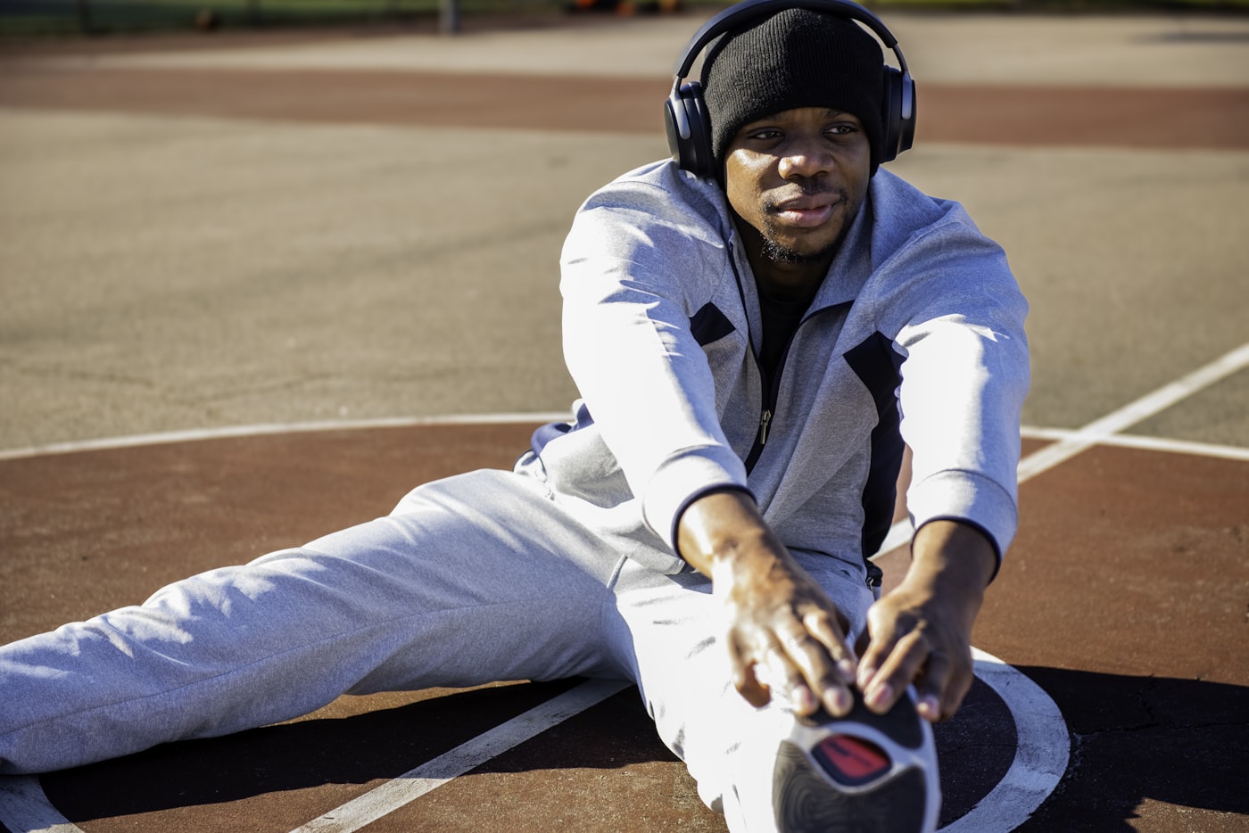 Man sitting on a tennis court wearing headphones, representing athletic recovery
