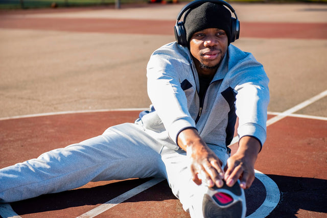 Man sitting on a tennis court wearing headphones, representing athletic recovery