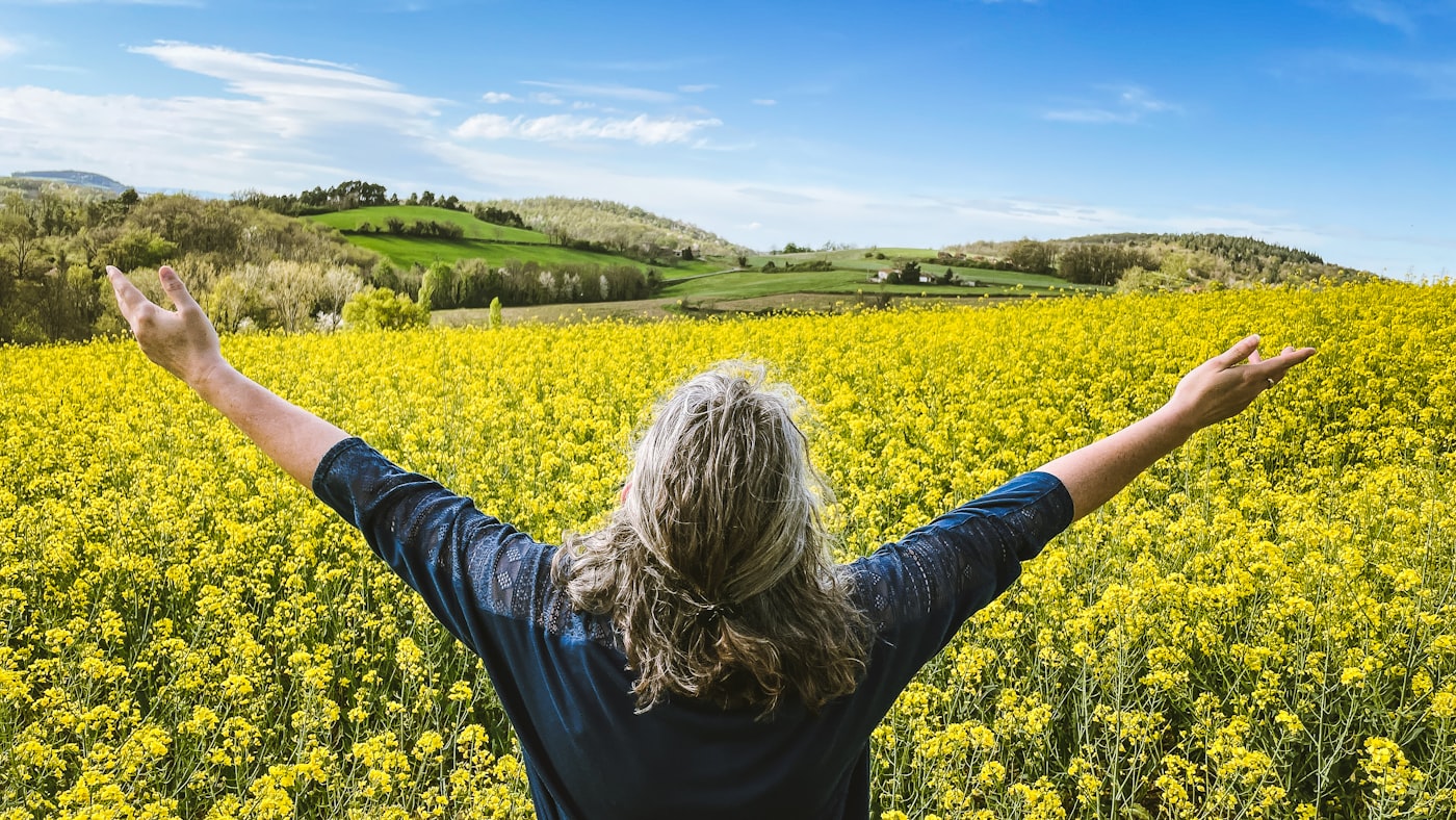 Woman embraces a field of yellow flowers.