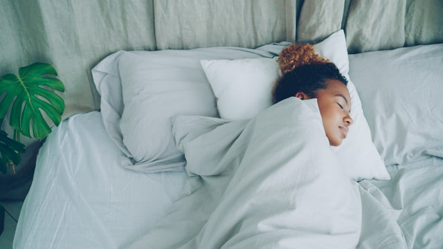 Woman sleeping peacefully in soft blue-grey bedding representing restorative sleep and hormone health