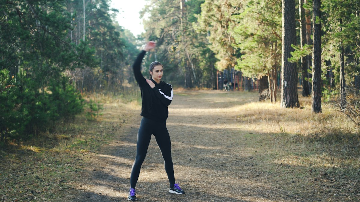 Woman stretching outdoors on forest path in athletic wear