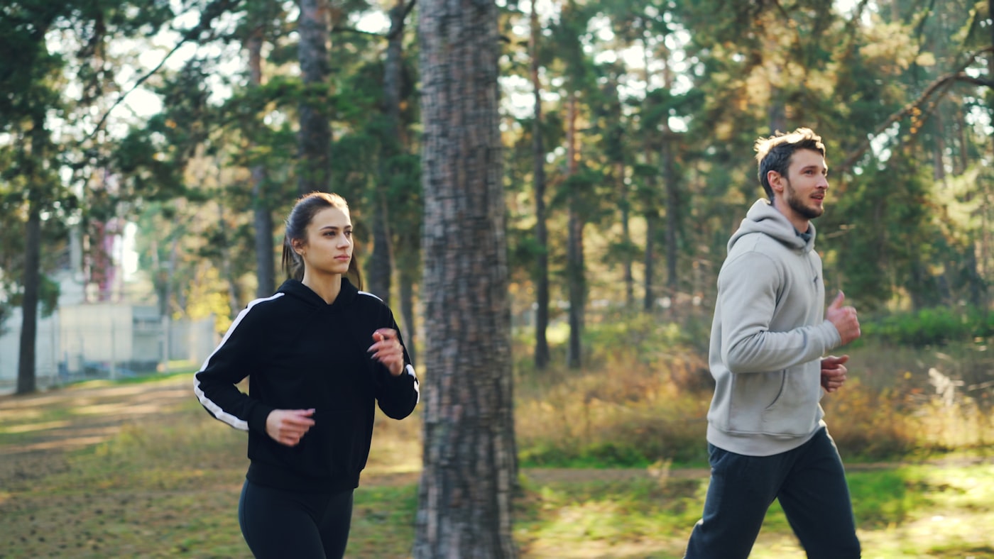 A man and woman jogging together on a forest path in natural light