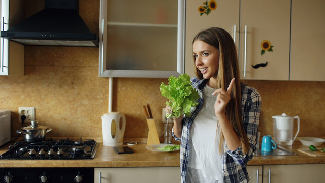 Young woman holding fresh lettuce in a kitchen, representing healthy nutrition