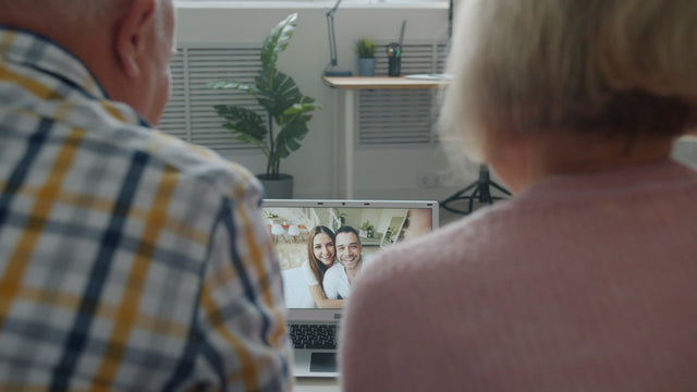 Elderly couple watches young couple on screen.