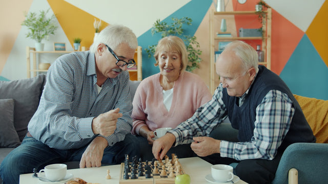 Three seniors playing chess together in a living room.