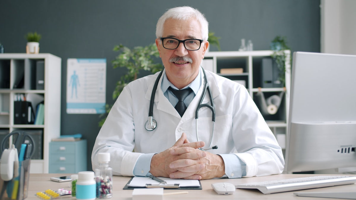 Elderly doctor in white coat with stethoscope at desk