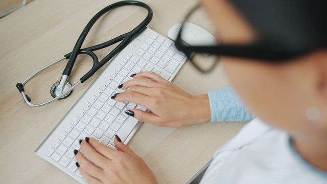 Doctor typing on keyboard with stethoscope nearby