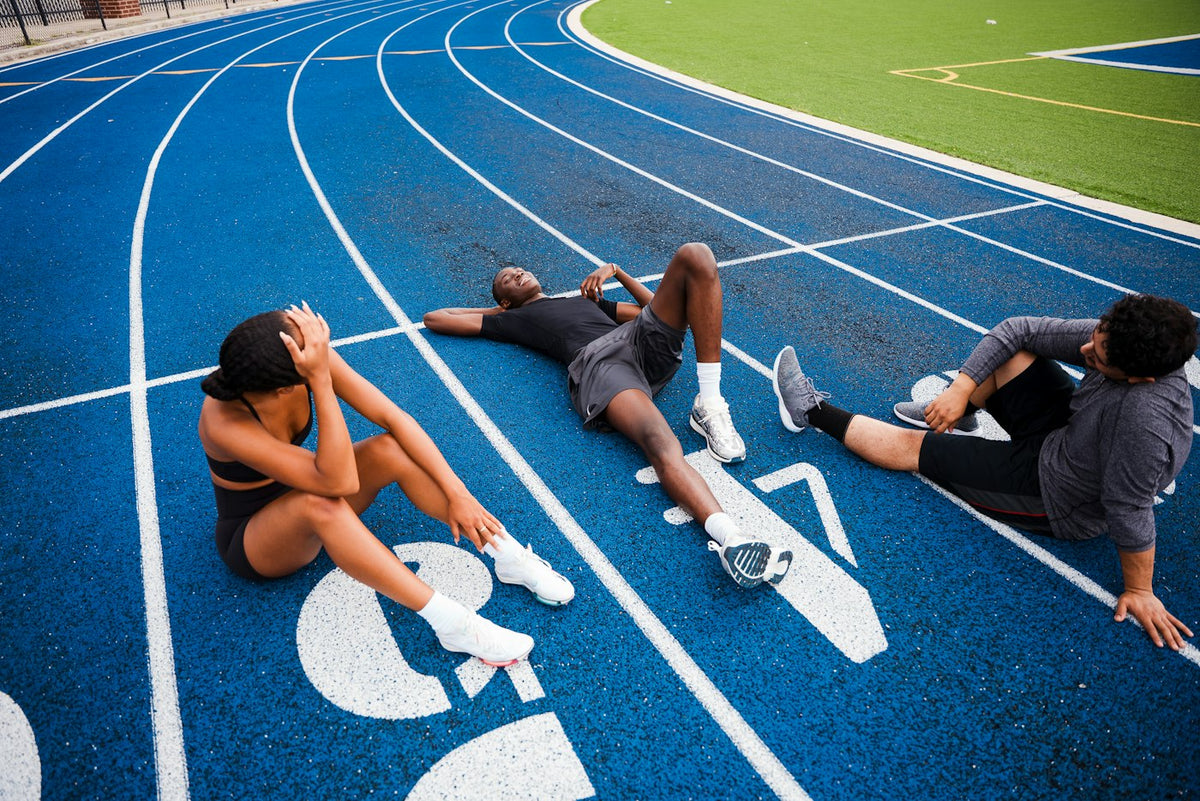 Three athletes resting and recovering on a blue running track after a workout