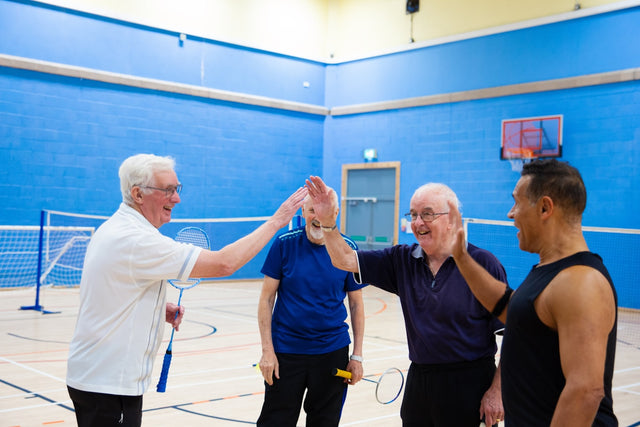 Four men playing badminton and giving high fives.