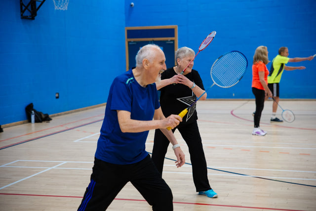 Seniors playing badminton in a gymnasium.
