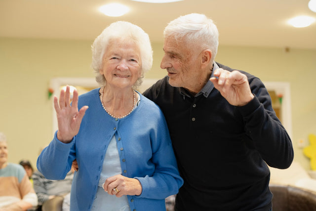 Elderly couple waving hello in a room