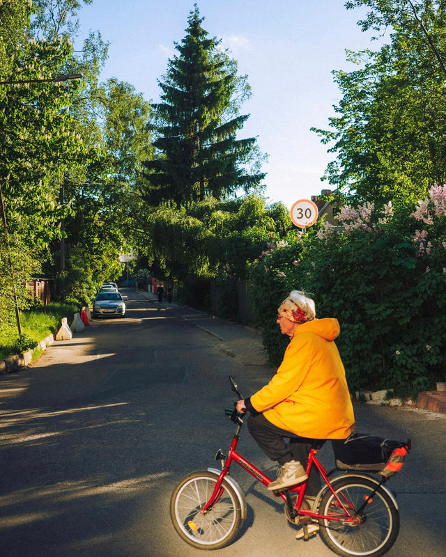 Older person in yellow jacket rides red bicycle on street.