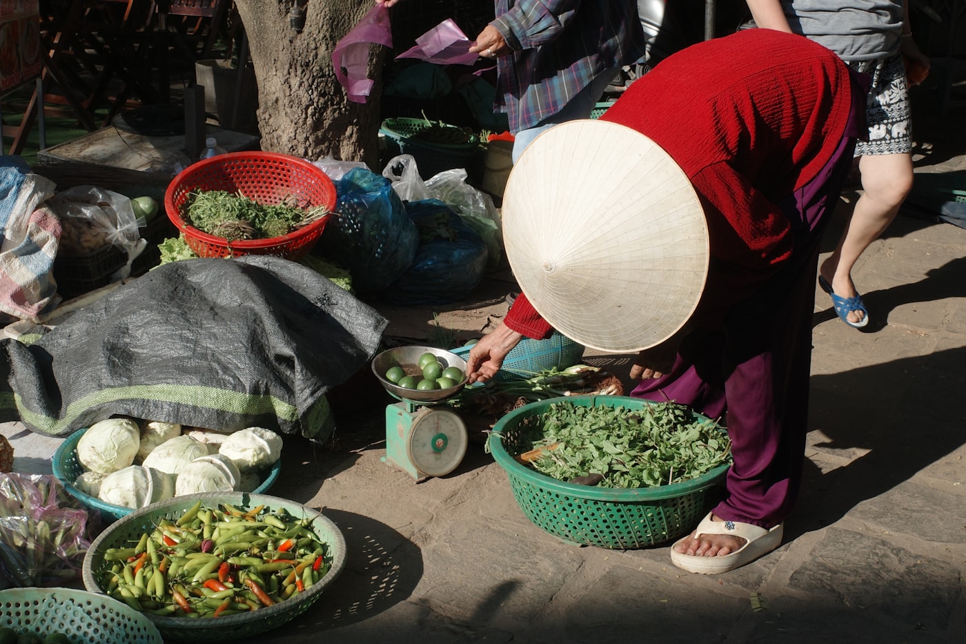 Vendor in conical hat sells fresh produce at a market.