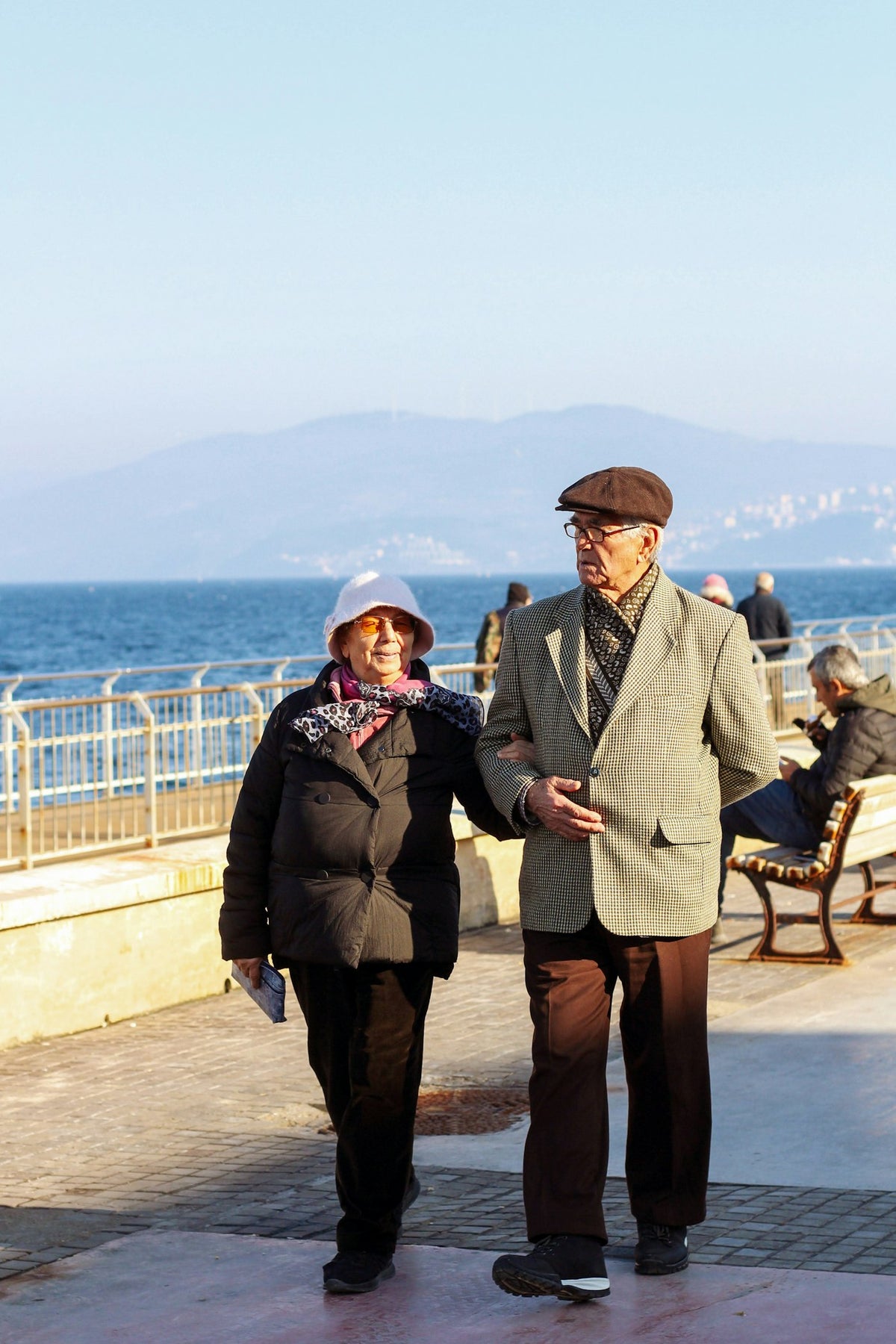 Older couple walking arm in arm along a sunny seaside promenade, illustrating healthy brain aging for an article on semaglutide and Alzheimer's research