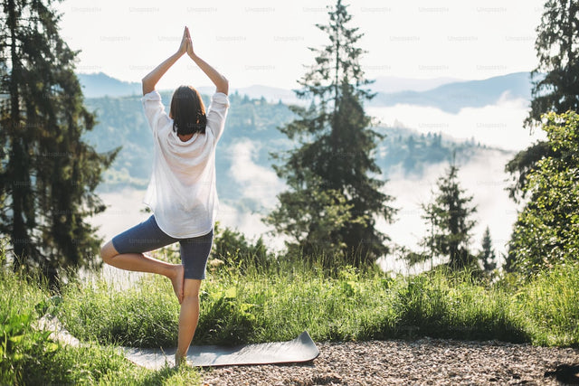 Woman practicing yoga in a mountain meadow at sunrise — wellness and stress management